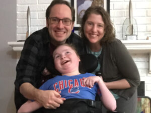 photo of the Thomases. Caitlin is in front wearing a blue Chicago Cubs shirt with red lettering. Michael ad Lynne are behind her. Everyone has broad smiles
